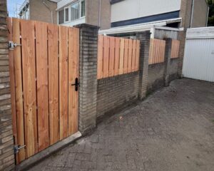 Houten schutting met poort op bakstenen muurtje