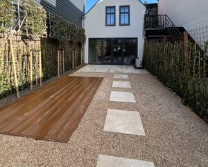 Tuin met vlonder, grindpad en tegelpaden tussen hagen