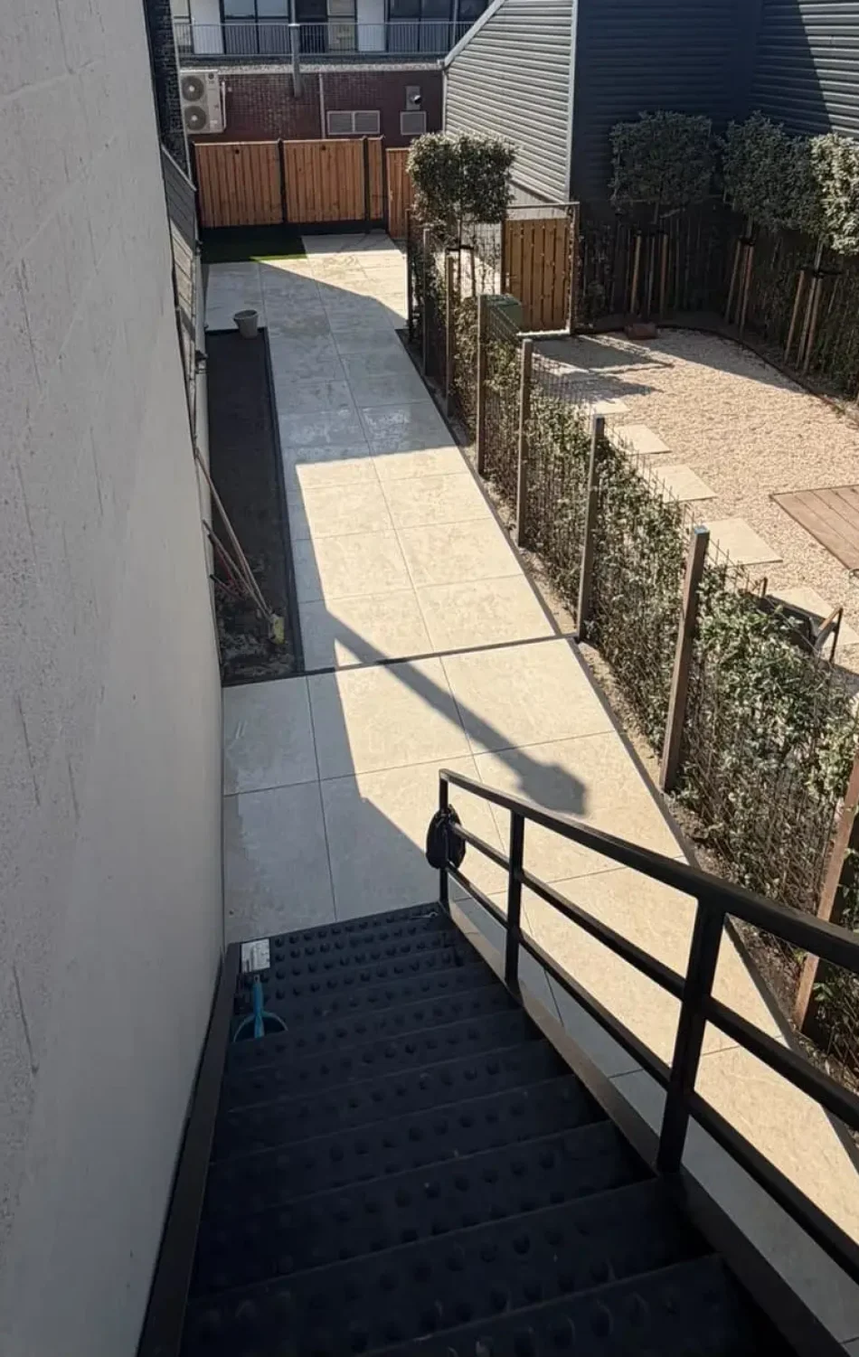 Tuin met grindpad, vlonder en hagen tussen twee woningen