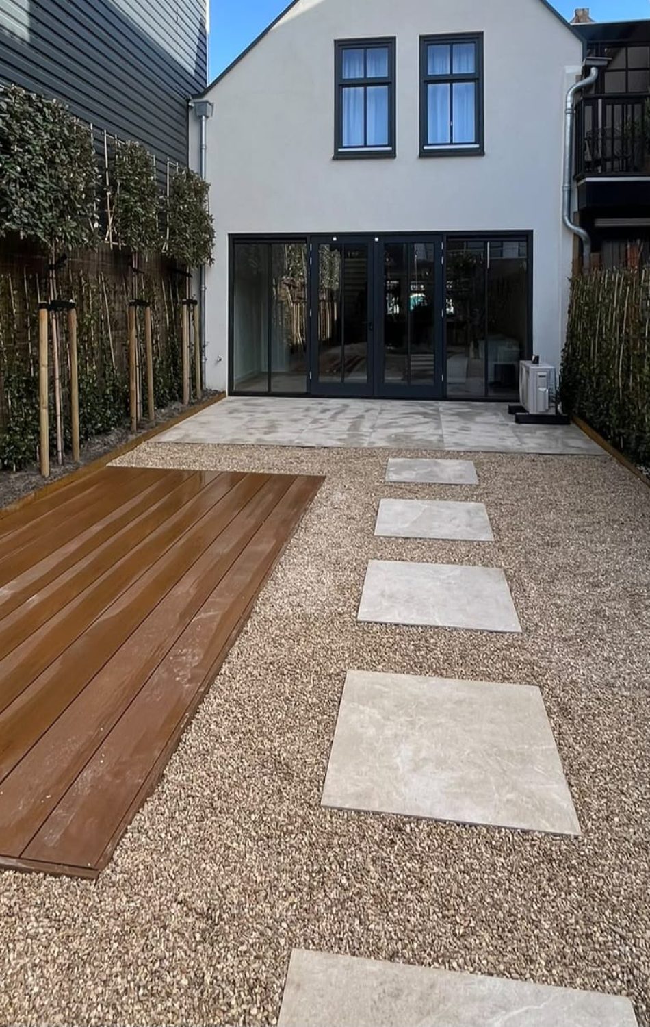 Tuin met vlonder, grindpad en tegelpaden tussen hagen